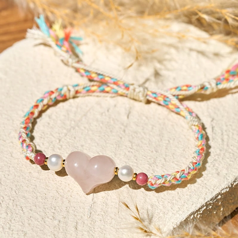 Pink Crystal Red String Bracelet With Tassel Ends On Beige Mat With Dried Grass