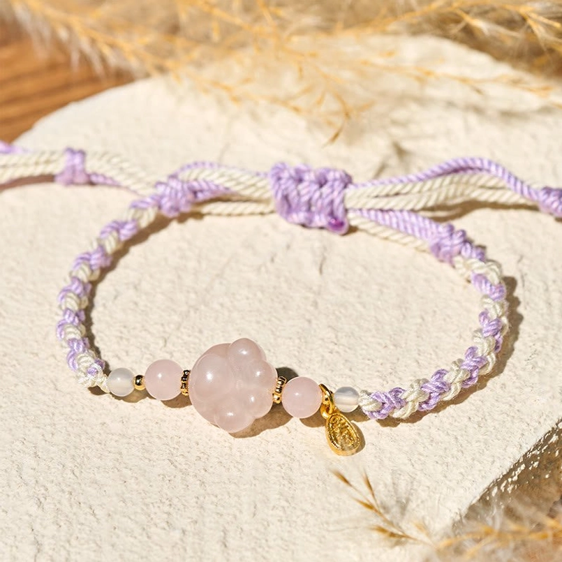 Side view of pink crystal cat claw bracelet with gold charm on linen background