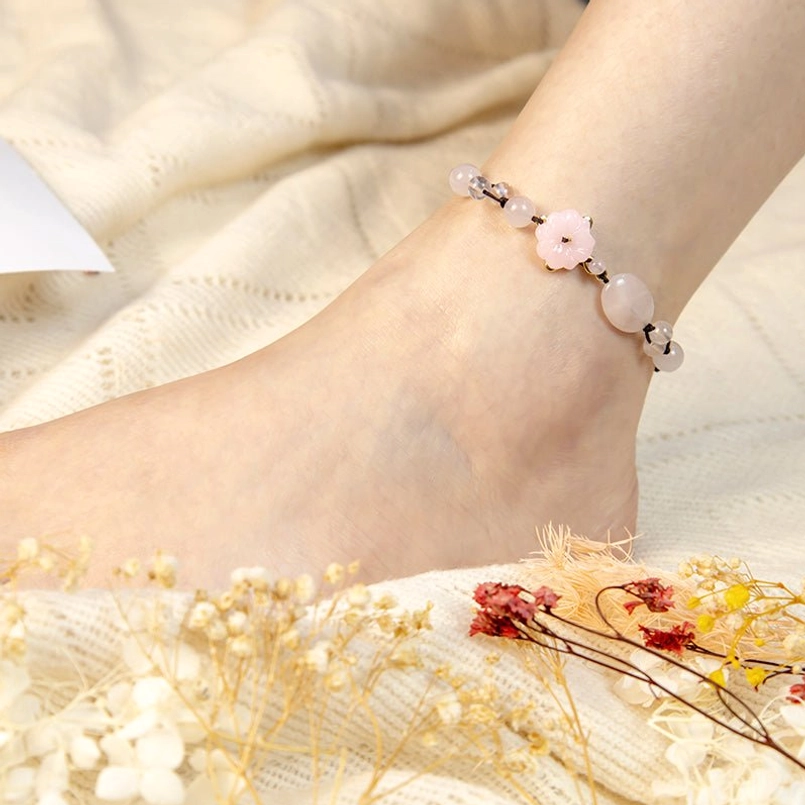 Close-up side view of pink crystal anklet worn on ankle with dried flowers background