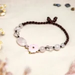 Pink crystal flower anklet flat lay with gold accents and braided cord on dark surface