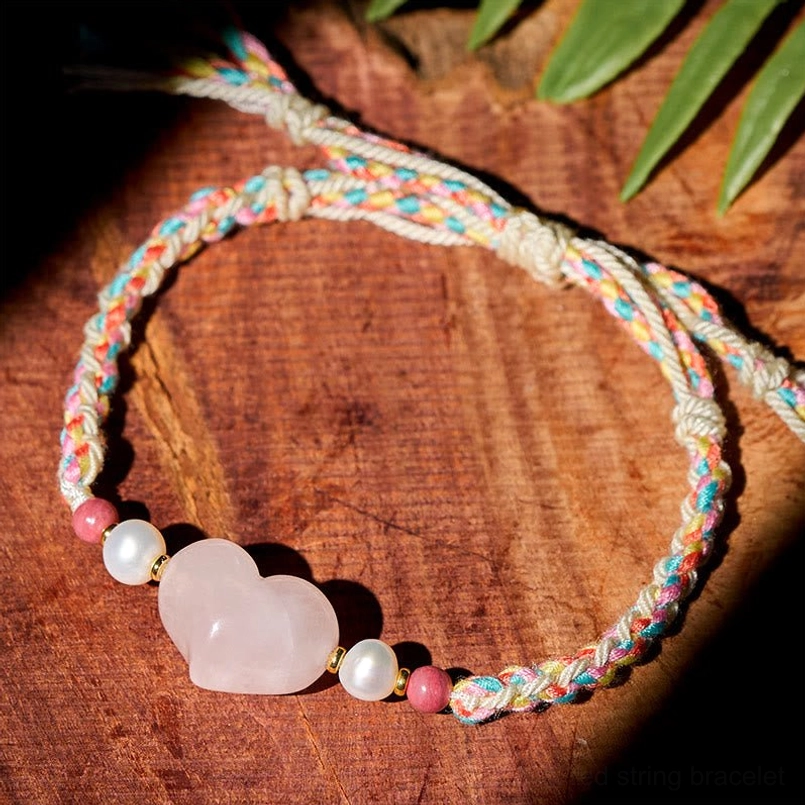 Pink Crystal Heart Red String Bracelet Flat Lay On Wooden Surface With Green Leaves