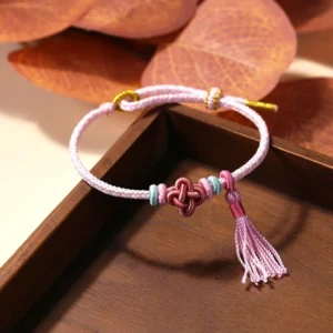 Pink Peach Blossom Knot Tassel Red String Bracelet top view on wooden tray