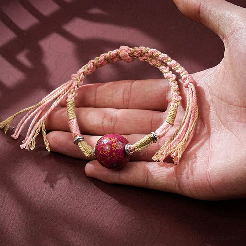 Light pink red string bracelet worn on hand with patterned lacquer bead