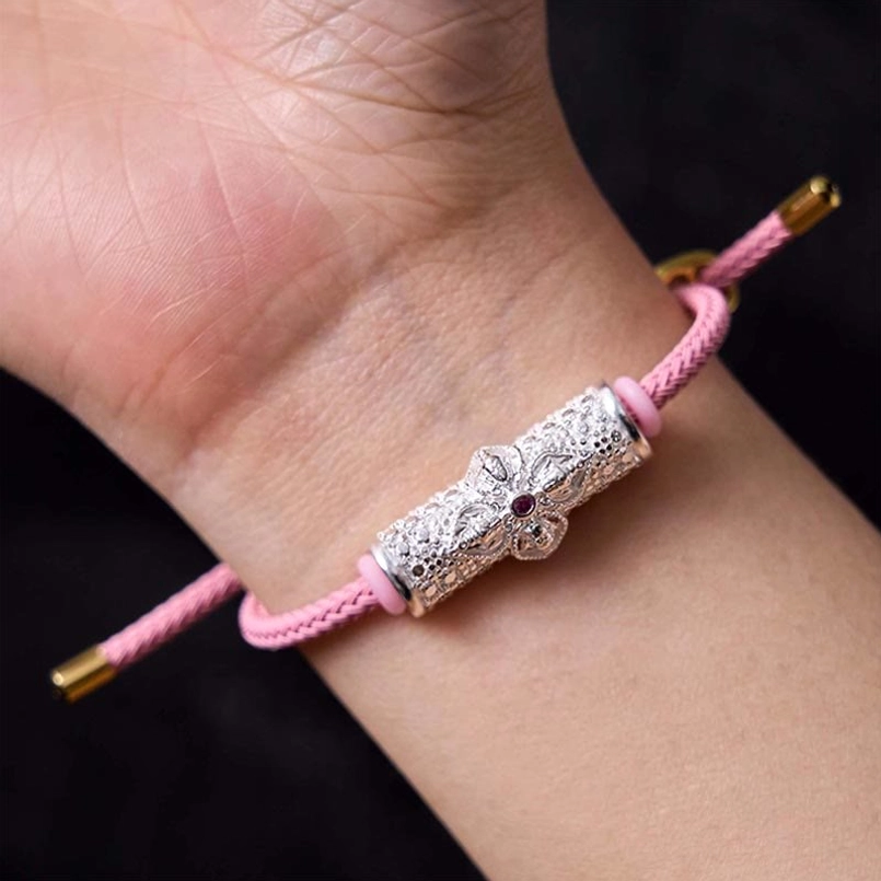 Pink string bracelet variant showing copper flower bead with natural fiber quality