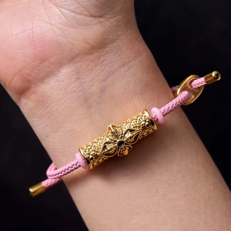Pink string protection bracelet with gold tone metal and colorful enamel flower