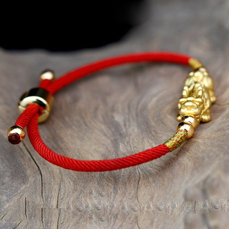 Close-up side view of Pixiu charm with gold plating and red woven rope