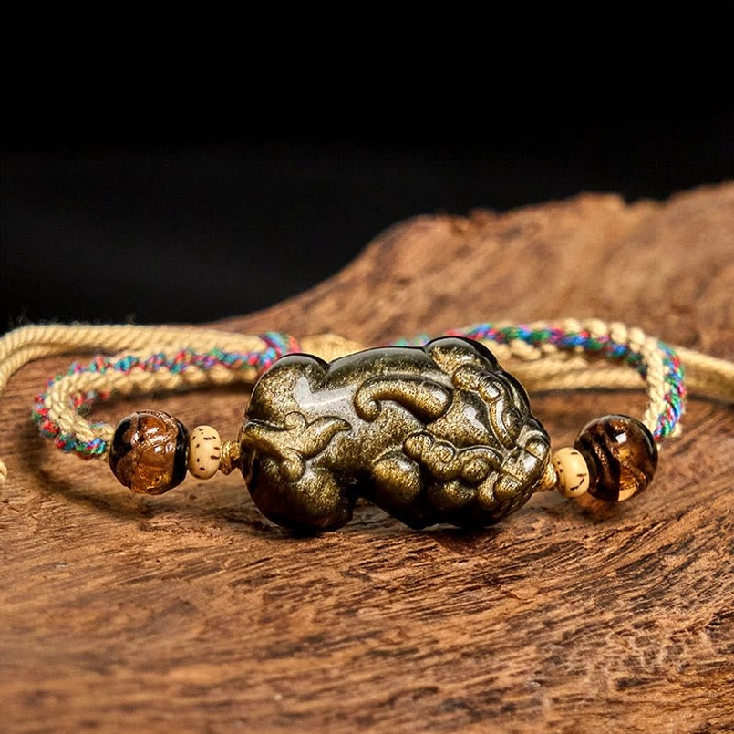 Close-up view of Gold Sheen Obsidian PiXiu bracelet laid flat on wooden surface showing colorful braided rope detail