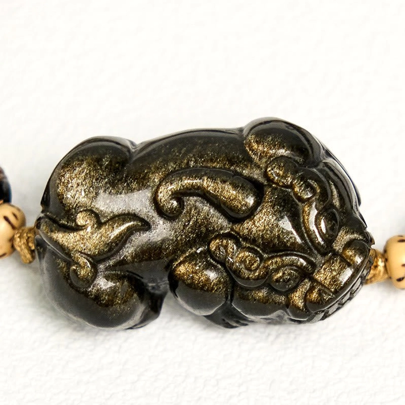 Front view of single Gold Sheen Obsidian PiXiu charm with carved details on white background