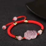 Pixiu pink crystal wealth bracelet with red string and gold spacers on dark background
