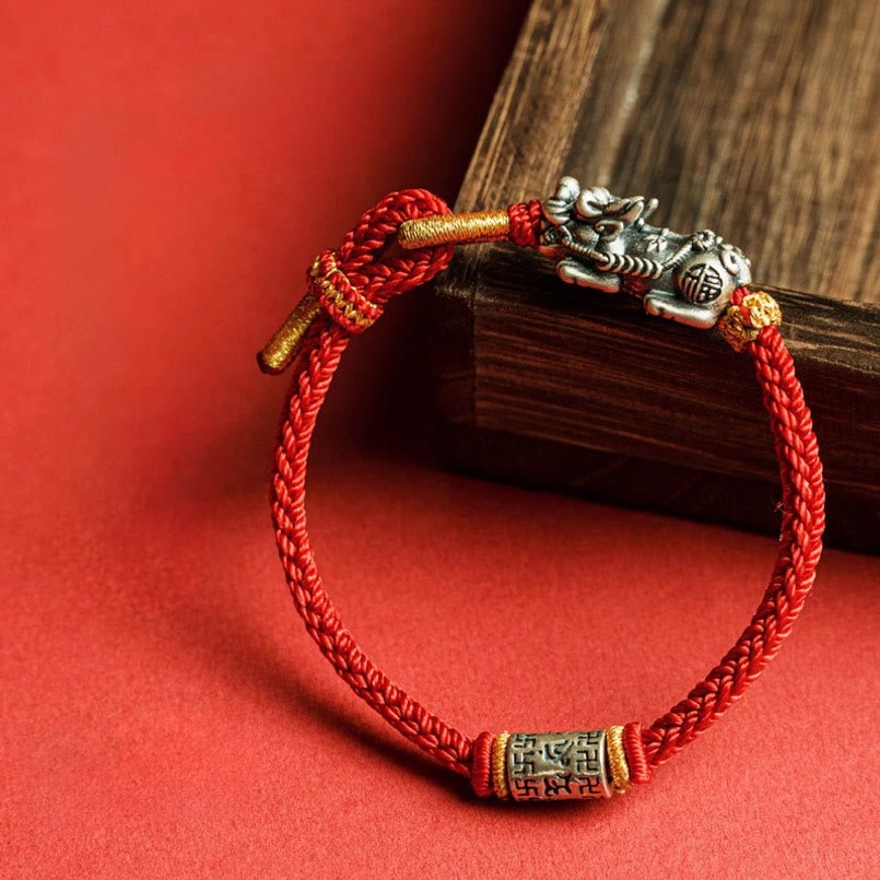 Sterling silver Pixiu protection string bracelet leaned on wooden block with gold-tipped rope ends detail