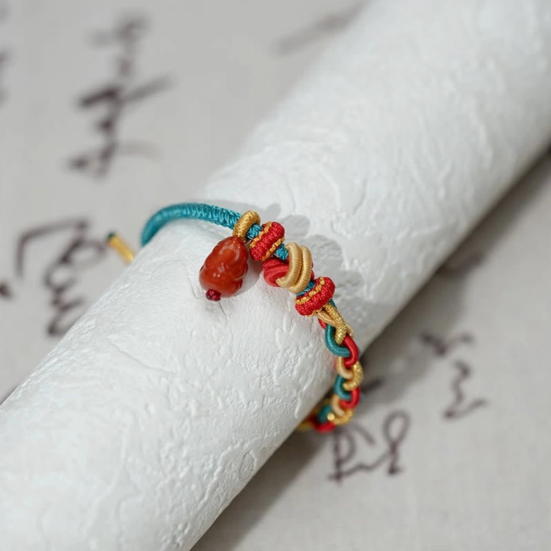 Close up side view of Pixiu charm braided red string bracelet on vintage calligraphy paper
