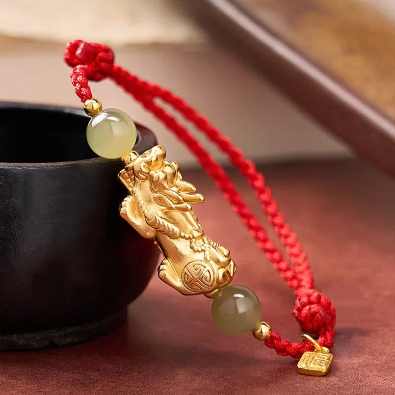 Close up side view of Pi Xiu Fu charm red string bracelet next to black ceramic cup