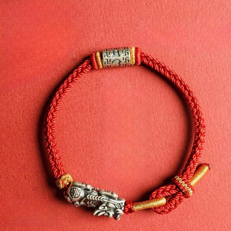 Red string Pixiu bracelet with mantra bead and silver charm front flat lay on solid red background