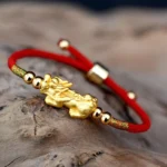 24K gold-plated Pixiu red string bracelet with adjustable design on rustic wooden surface