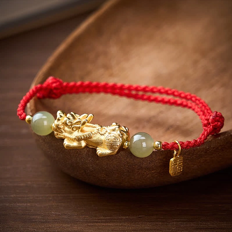 Three quarter side view of Pi Xiu red string bracelet in wooden bowl on wooden table