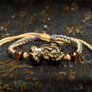 Gold Sheen Obsidian PiXiu wealth bracelet displayed overhead with braided rope on dark background with Chinese patterns
