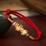 Copper Pi Xiu red string wealth bracelet on dark wooden table with jade beads and gold charm details