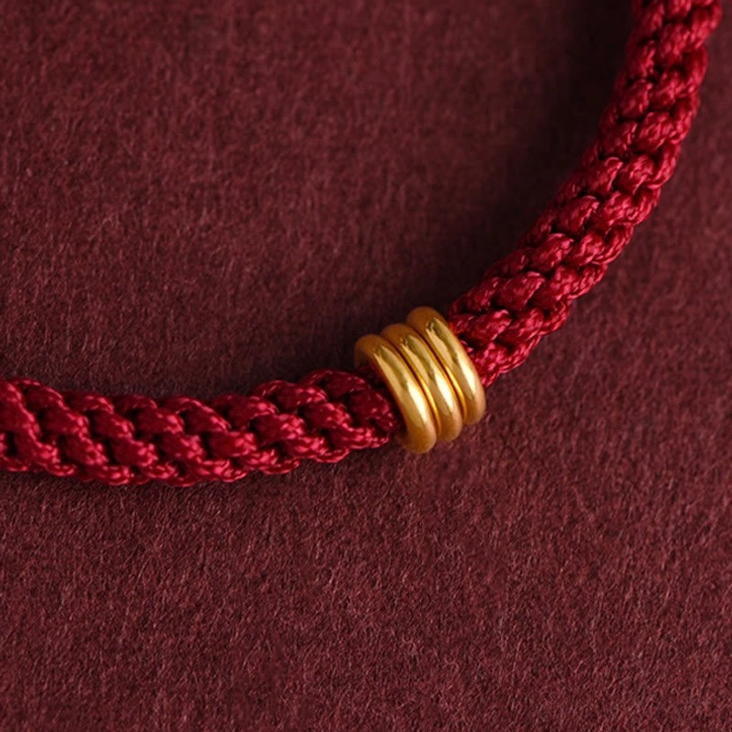 Polished 999 gold triple ring accent on handmade red braided bracelet macro