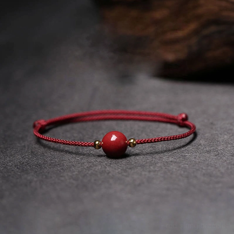 Red braided string cinnabar bead bracelet with metal spacers on gray fabric background