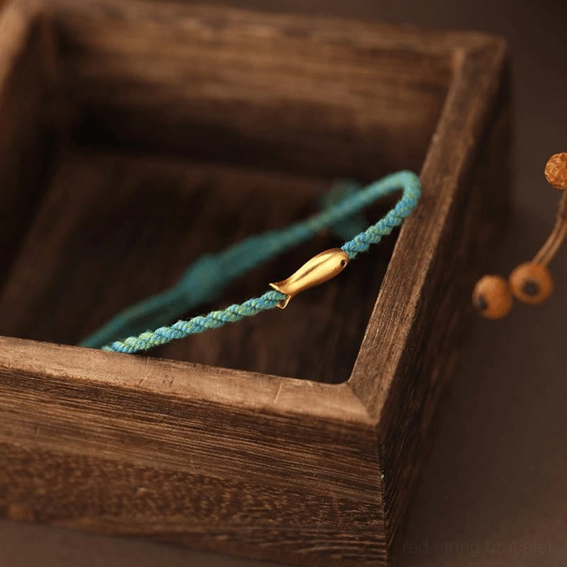 Turquoise cord koi fish bracelet with gold charm displayed in wooden box with decorative elements