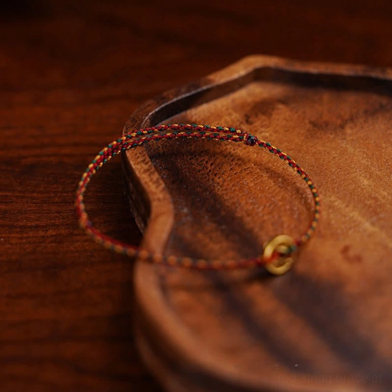 Braided protection bracelet with copper coin charm viewed from side angle on wooden tray