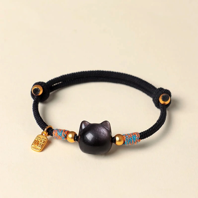 Top-down view of silver sheen obsidian cat protection bracelet with gold-toned Fu symbol charm on light pink background