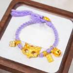 Purple string fox bell bracelet with Fu character 24k gold plated charm displayed on wooden tray