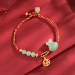 Year of the Rabbit Hetian jade red string bracelet with silver charm on red silk flat lay