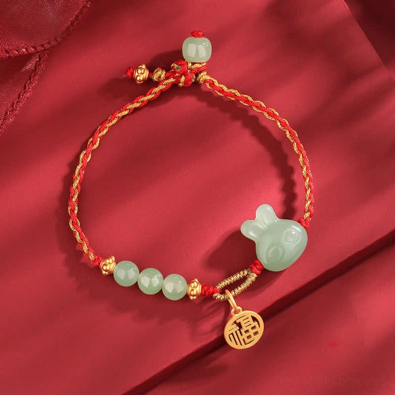Year of the Rabbit Hetian jade red string bracelet with silver charm on red silk flat lay