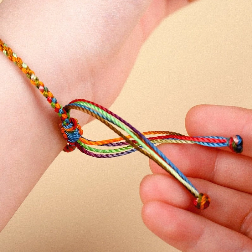 Hand-held close-up view of rainbow braided bracelet showing adjustable knot and colorful silk threads