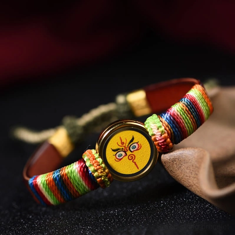 Rainbow woven Tibet wealth gods bracelet with yellow Buddha charm on wooden stand