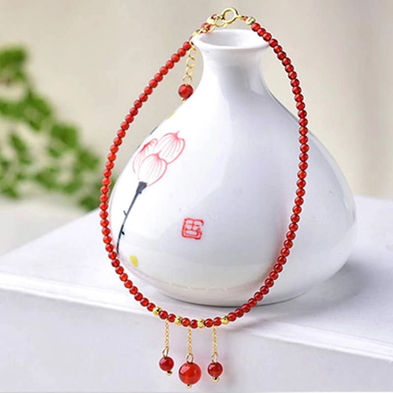 Red agate anklet hanging shot with ceramic vase showing gold accents and multiple dangling beads