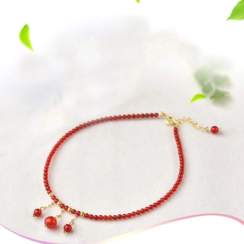 Red agate anklet with thin beads and gold hardware on greenery decorated surface