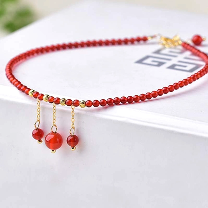 Red agate anklet chain with triple dangling pendants on patterned surface