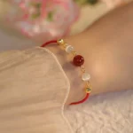 Red agate cat eye confidence bracelet worn on wrist with red string and gold hardware