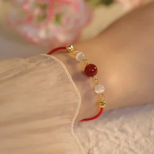 Red agate cat eye confidence bracelet worn on wrist with red string and gold hardware
