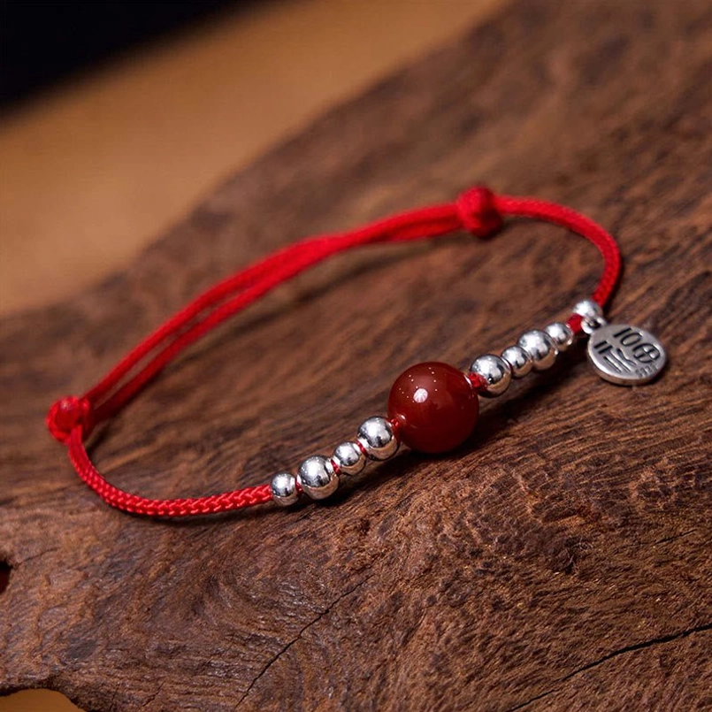 Close-up of red agate bead and double-sided silver Fu charm on braided bracelet