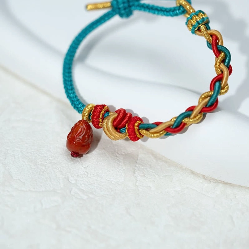 Close up front view of dangling red agate Pixiu pendant on braided red string bracelet