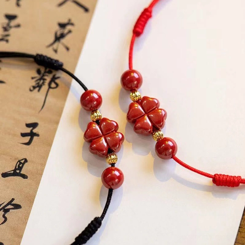 Red and black cinnabar anklet set with four leaf clover charms on calligraphy background