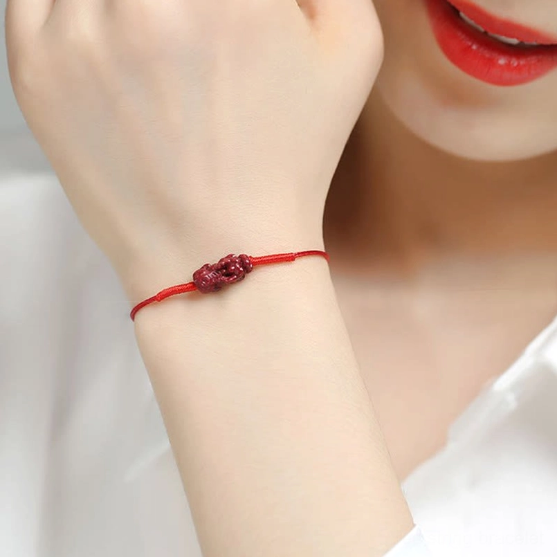 Red blessing bracelet worn on wrist with charm detail