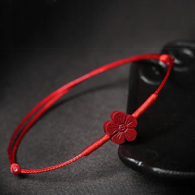 Red cord bracelet with plum blossom cinnabar bead on display stand