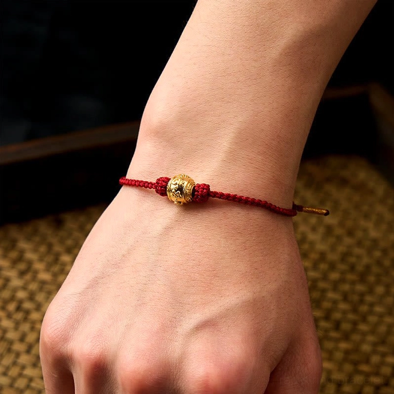 Red string protection bracelet worn on wrist showing slim braided rope and gold mantra bead