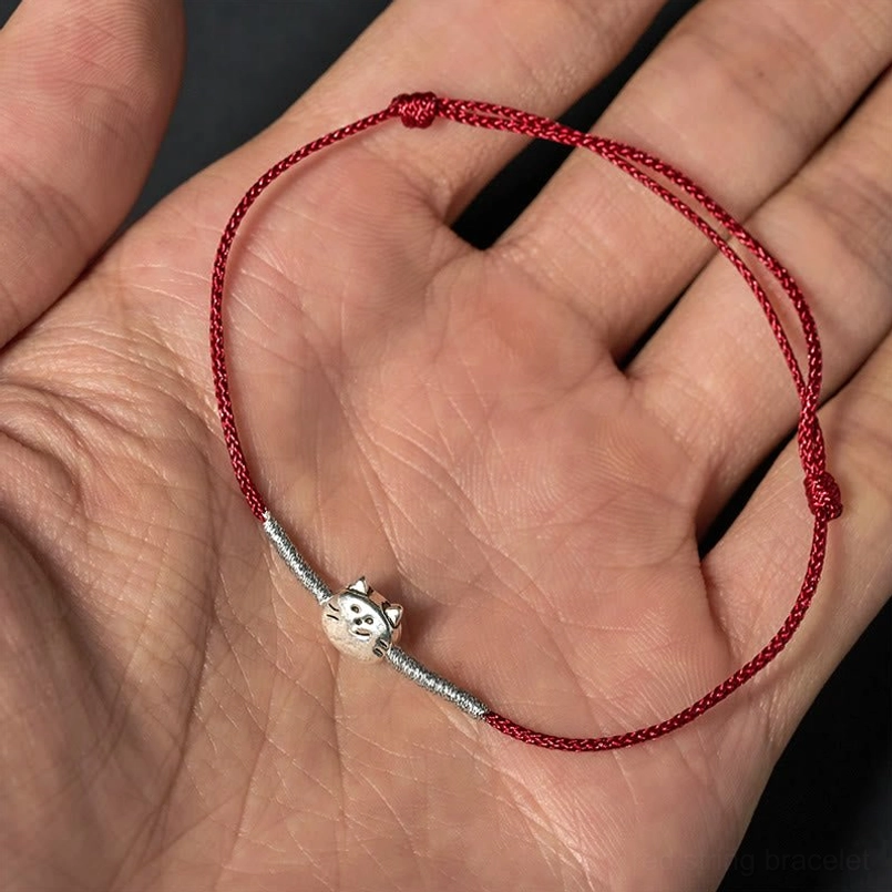 Double-layer red woven cat charm bracelet with silver accents on palm background
