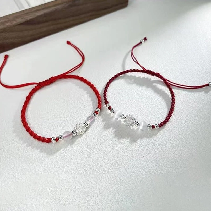red braided string bracelet with silver lotus and cat's eye beads on wooden table