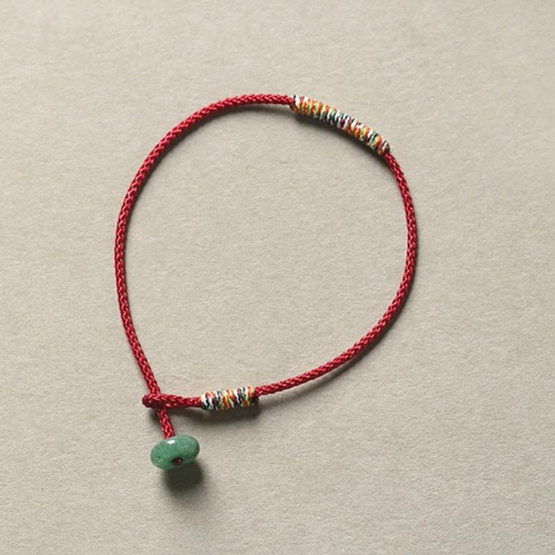 Red braided lucky bracelet with green aventurine pendant and colorful beaded details on neutral background