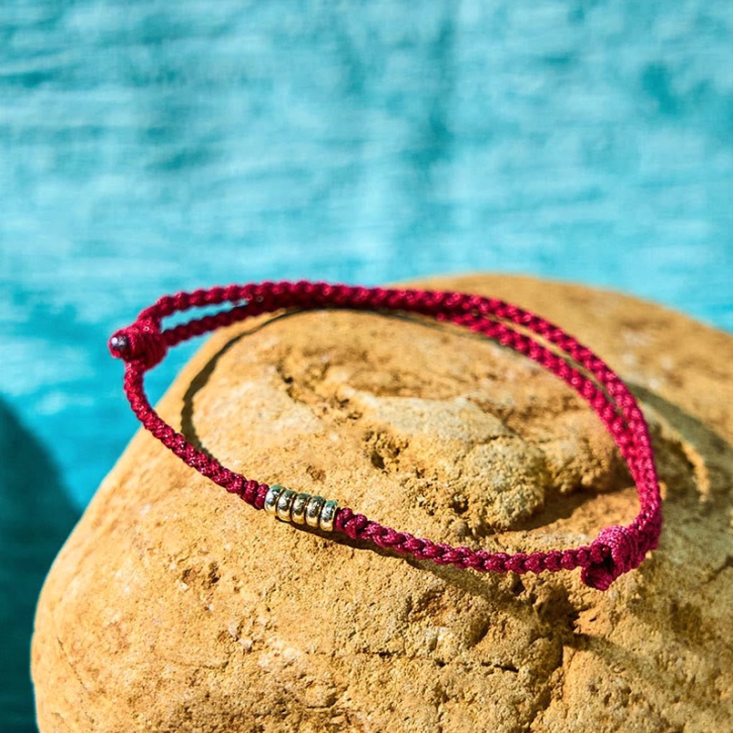 Red braided string bracelet with silver beads displayed on stone background