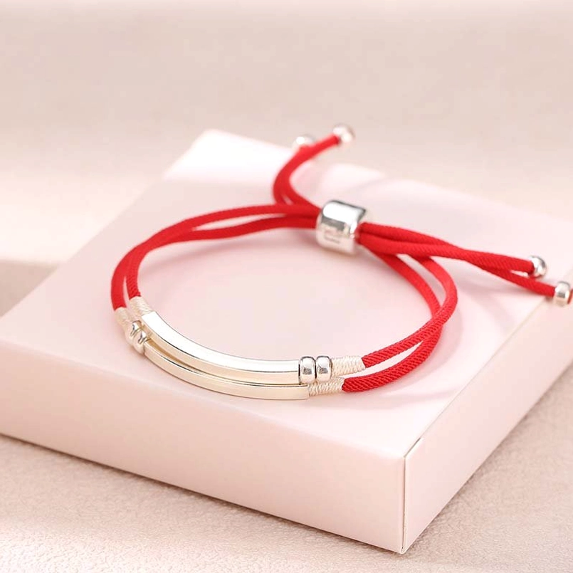Red braided cord bracelet with dual silver accent bars and sliding lock closure on pink display box