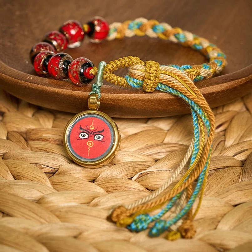 Red beaded Tibetan Buddha eye bracelet low angle view on natural background with tassel detail