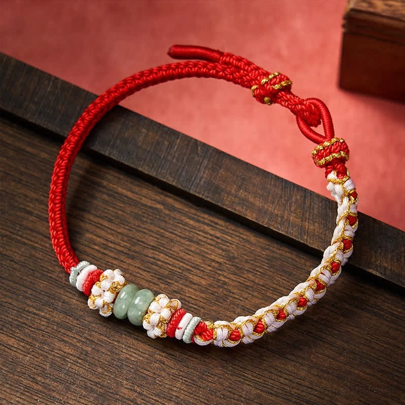 Red Chinese knot jade bracelet with peach blossom details handmade on wooden surface