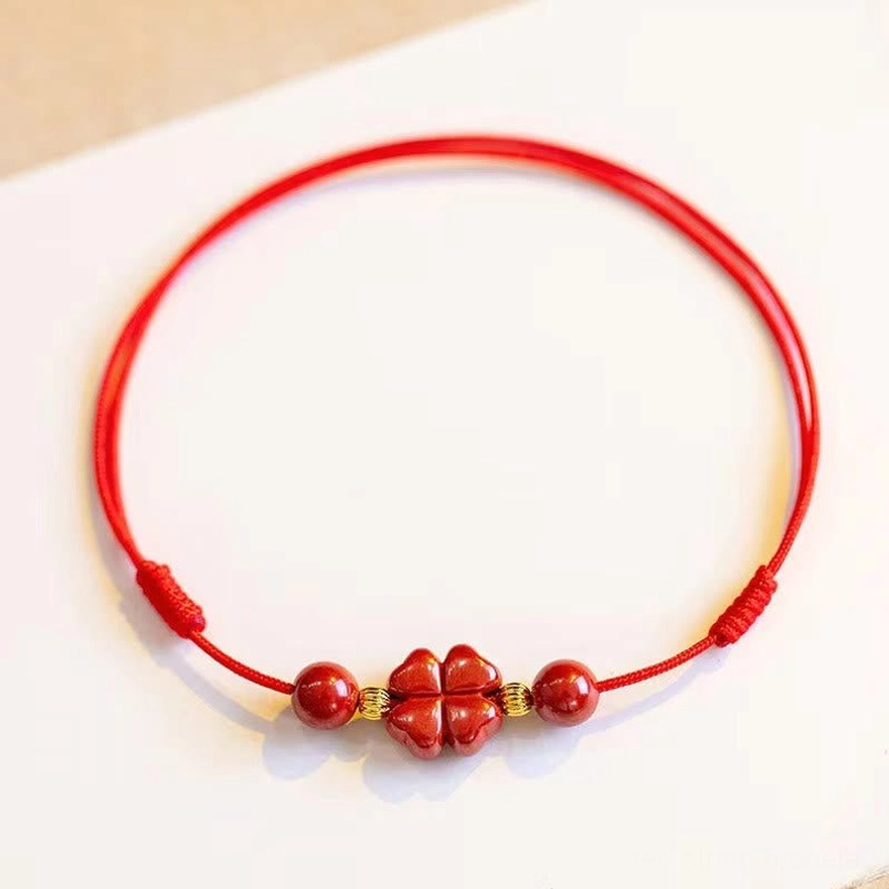 Red string cinnabar anklet flat lay overhead view showing four leaf clover charm and round beads